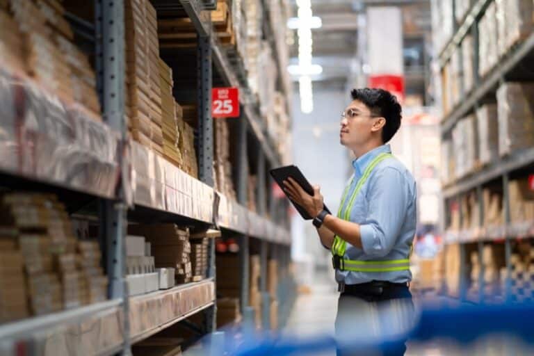 Warehouse worker in security uniform with tablet computer looking at merchandise in large warehouse Logistics and export business Logistics distribution center